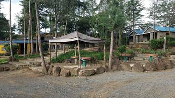 Un espacio al aire libre rústico con mesa y sillas de madera, rodeado de rocas y vegetación.