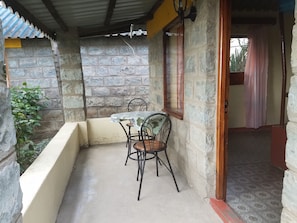 Un petit espace extérieur aménagé avec une table et des chaises, des murs en pierre et une fenêtre avec un rideau.