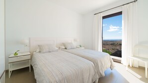 A bedroom with two beds, a nightstand, a bedside table, and a view of the landscape through the window.