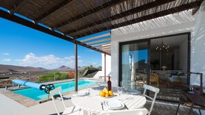 A poolside area with a table set for dining, a bottle of wine, and a view of the pool and mountains.