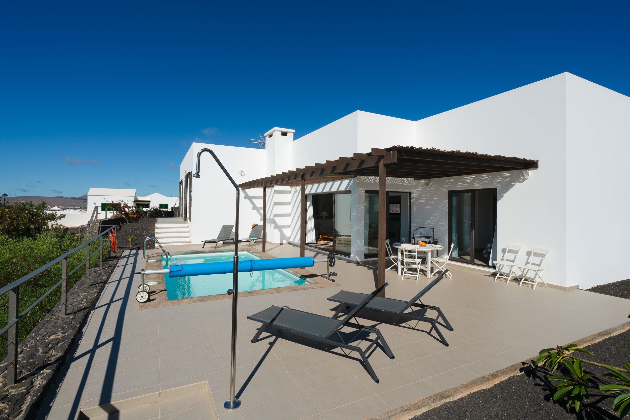 Un área de piscina moderna al aire libre con un pérgola, sillones de descanso y una mesa de comedor.