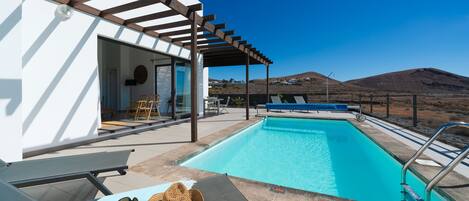 Un espace aménagé au bord de la piscine, avec une pergola, des chaises longues et une vue sur le paysage.