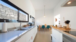 A modern kitchen with a stone wall, a sink, a stove, and a dining area with chairs.