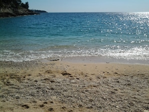 A beach with clear water, pebbles, and a distant shoreline.