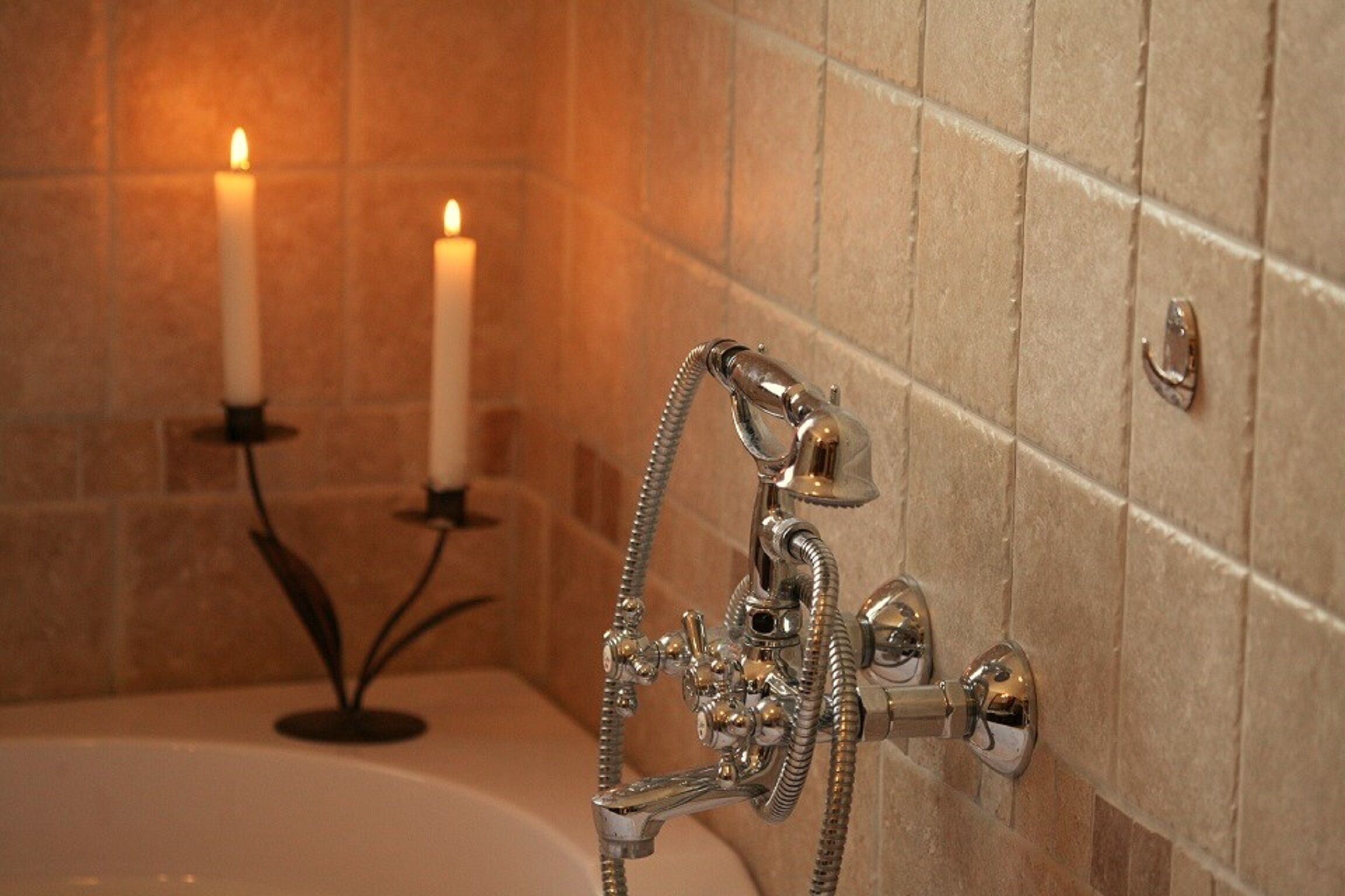 Ein Badezimmer mit einer Badewanne, einem Duschkopf und zwei brennenden Kerzen auf einem Sockel.