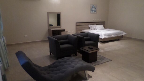 A modern bedroom with a bed, two armchairs, a small table, and a mirror. - Gloriana Apartments (Abuja)
