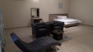 A modern bedroom with a bed, two armchairs, a small table, and a mirror.