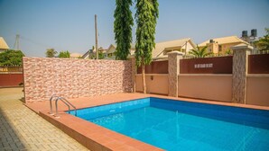 A rectangular swimming pool with a tiled edge, surrounded by a brick wall and a metal fence. - Gloriana Apartments (Abuja)