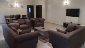 A modern living room with a sofa set, a coffee table, and a flat-screen TV mounted on the wall. - Gloriana Apartments (Abuja)