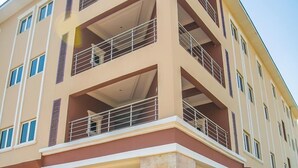 A multi-story hotel with a central entrance, balconies on each floor, and a brick-paved courtyard. - Gloriana Apartments (Abuja)