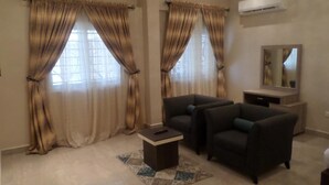 A living room with two armchairs, a small coffee table, and a television on a stand. - Gloriana Apartments (Abuja)