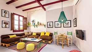 A cozy living room with a brown sofa, yellow cushions, a coffee table, and a dining area with a green chair and a small table.