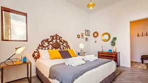 Habitación de hotel con una cama grande, una mesita de noche con lámpara, un aparador y un espejo en la pared.