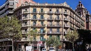 Un edificio de varios pisos con balcones, un reloj y un toldo a rayas rojas y blancas.