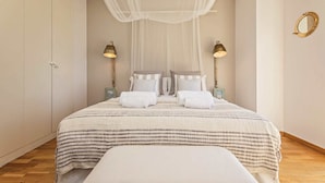 Ein Schlafzimmer mit Bett, Nachttischlampen, einer Bank und einem Baldachin.