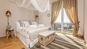 Ein Schlafzimmer mit einem großen Bett, einem Nachttisch, einer Lampe, einem Fenster mit Vorhängen und Blick auf die Stadt.