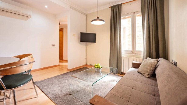 A modern living room with a glass coffee table, a sofa, a dining table with chairs, a flat-screen TV, and a window with curtains.
