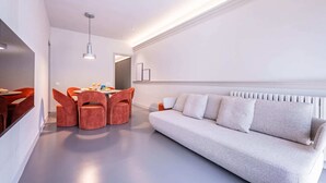 Uma sala de estar moderna com um sofá, uma mesa de jantar com cadeiras e uma luminária pendente.