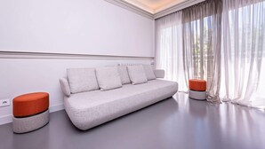 Uma sala de estar moderna com um sofá cinza, dois pufes vermelhos e cortinas leves.