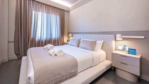 Quarto de hotel moderno com uma cama grande, uma mesa de cabeceira e um criado-mudo.