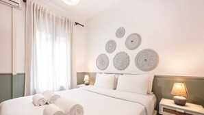 A hotel room with a neatly made bed, a bedside lamp, decorative wall art, and a window with curtains.