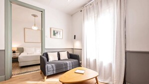 A modern hotel room with a grey sofa, a wooden coffee table, and a bed with white bedding.