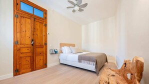 Een slaapkamer met een houten deur, een bed met hoofdeinde, een plafondventilator en een houten sculptuur.