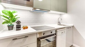 A modern kitchen with white cabinetry, a stainless steel microwave, a built-in oven, a sink with a faucet, and a potted plant.