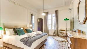 A hotel room with a large bed, a dresser, a mirror, and a view of the city through the windows.