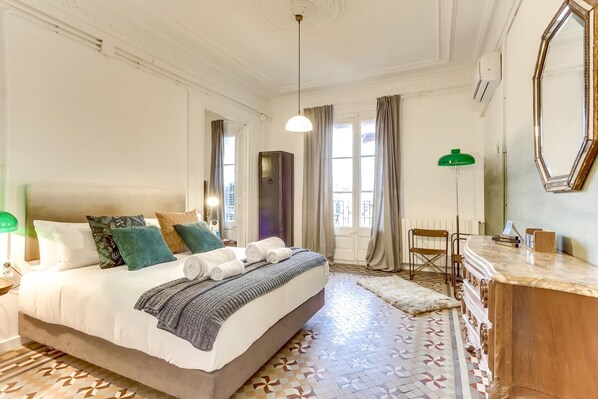 A hotel room with a large bed, a dresser, a mirror, and a view of the city through the windows.
