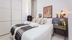 Une chambre d’hôtel comprenant un lit, une table de chevet, une horloge murale, une carte encadrée et une lampe.