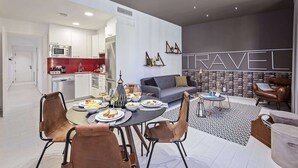 Un salon moderne avec un canapé gris, une table à manger avec des chaises et un coin cuisine doté de meubles blancs et de touches de couleur rouge.