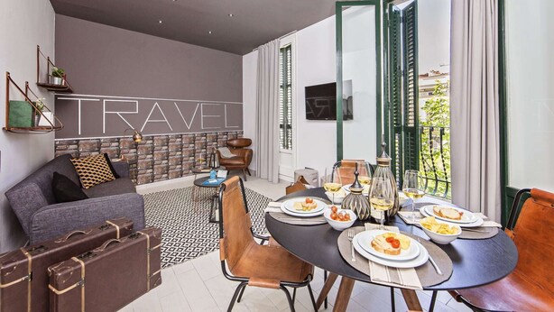 Un salon moderne avec un canapé, une table à manger dressée pour deux personnes et une grande fenêtre avec des rideaux.