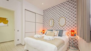 Ein modernes Schlafzimmer mit einer gepolsterten Kopfteil, einem großen Spiegel und einem Nachttisch mit Lampe.