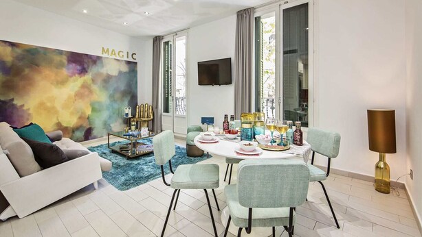 Ein modernes Wohnzimmer mit einem weißen Sofa, türkisfarbenen Kissen, einem Glastisch und einem farbenfrohen abstrakten Wandbild.
