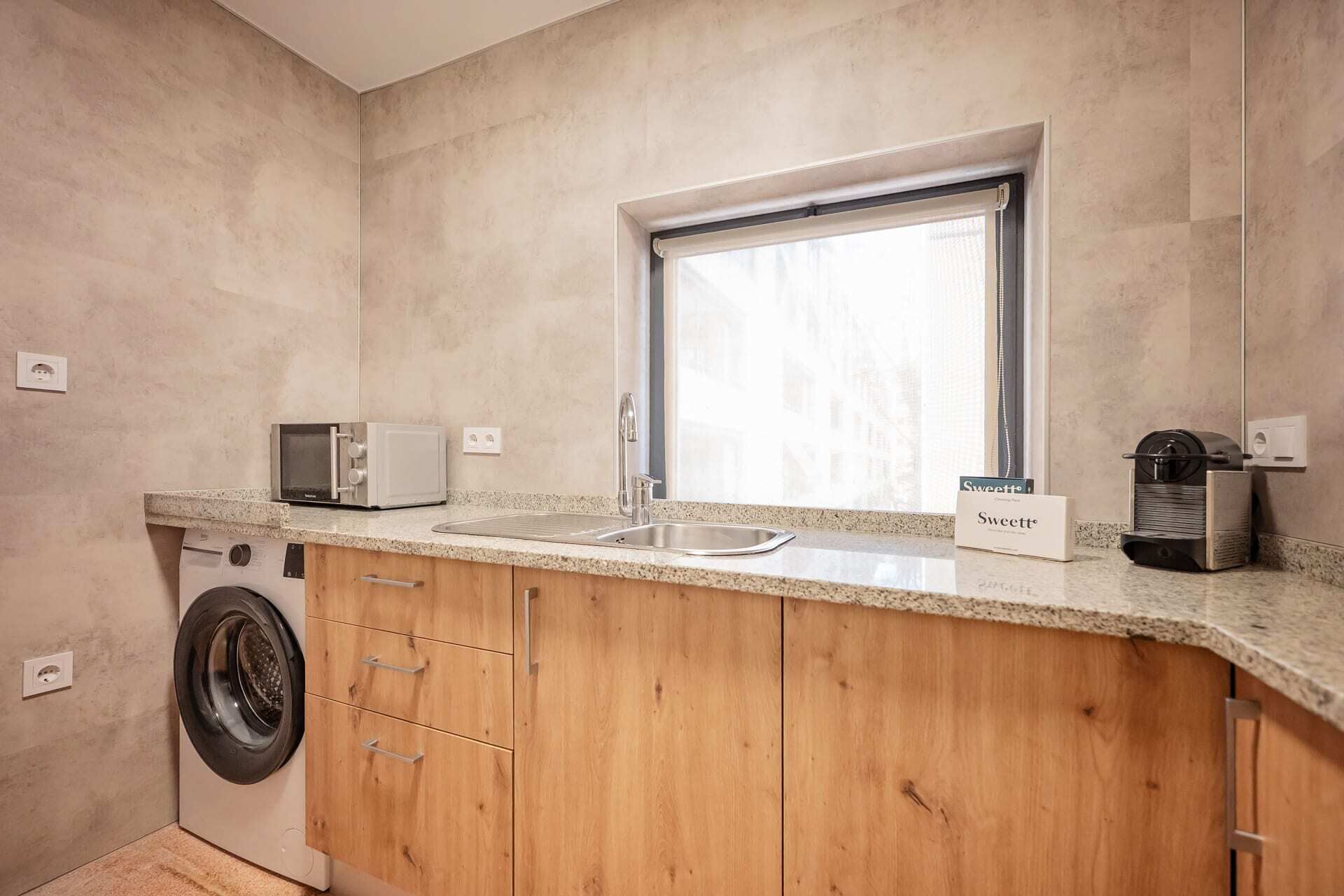 A compact kitchen with a washing machine, a microwave, a sink, and a window.