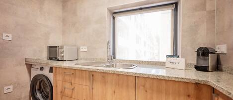 A compact kitchen with a washing machine, a microwave, a sink, and a window.