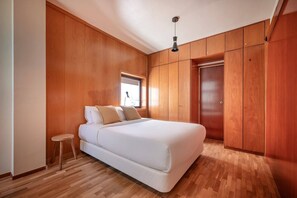 Une chambre avec un grand lit, des murs en bois, un petit tabouret et une armoire.