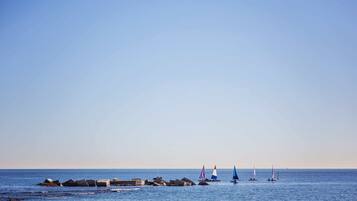 Une mer calme sous un ciel dégagé, une digue rocheuse et plusieurs voiliers.