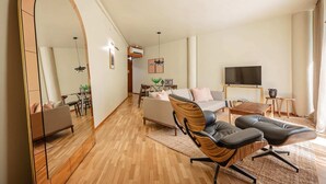 A spacious living room with a large mirror, a sofa, two armchairs, a TV, and a dining area with a table and chairs. - Sweett | Bogatell Beach (Barcelona)