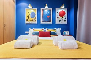 A hotel room with a blue accent wall, a bed with white and yellow bedding, and three framed artworks above the bed.