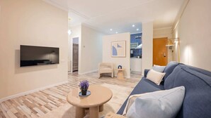A modern living room with a flat-screen TV, a sofa, a coffee table, and a kitchen area in the background. - Sweett | Charming in Sant Gervasi (Barcelona)