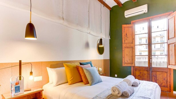 Habitación de hotel con cama, mesita de noche, lámpara y vista a edificios a través de la ventana.