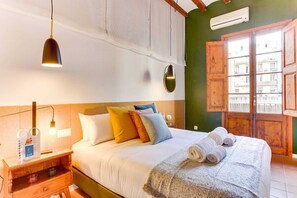 A hotel room with a bed, bedside table, lamp, and a view of buildings through a window.