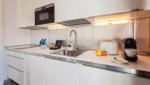 Una cocina moderna con un lavamanos de acero inoxidable, un horno empotrado y un tostador. Hay dos botellas de agua y una planta pequeña en la encimera.