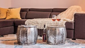 Ein gemütliches Wohnzimmer mit einem braunen Sofa, einer weißen Decke und zwei rustikalen Fässern als Beistelltischen.