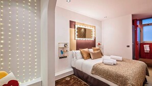 Ein modernes Hotelzimmer mit einem Bett, einem Schminktisch mit Beleuchtung, einer Uhr und einem Fenster.