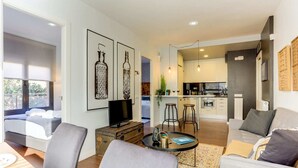 A modern living room with a sofa, a coffee table, and a TV. There is a kitchen in the background with a dining area. - Sweett | Raul - Two Bedroom Apartment, Sleeps 4 (Barcelona)