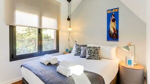 A modern bedroom with a large bed, a window with a view, a poster on the wall, and a bedside table with a lamp. - Sweett | Raul - Two Bedroom Apartment, Sleeps 4 (Barcelona)