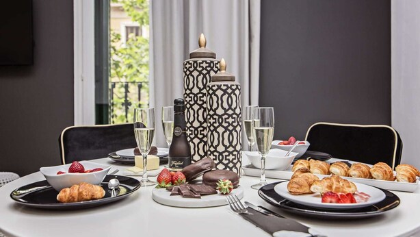 A dining table set with plates of croissants, strawberries, chocolate, and glasses of champagne.